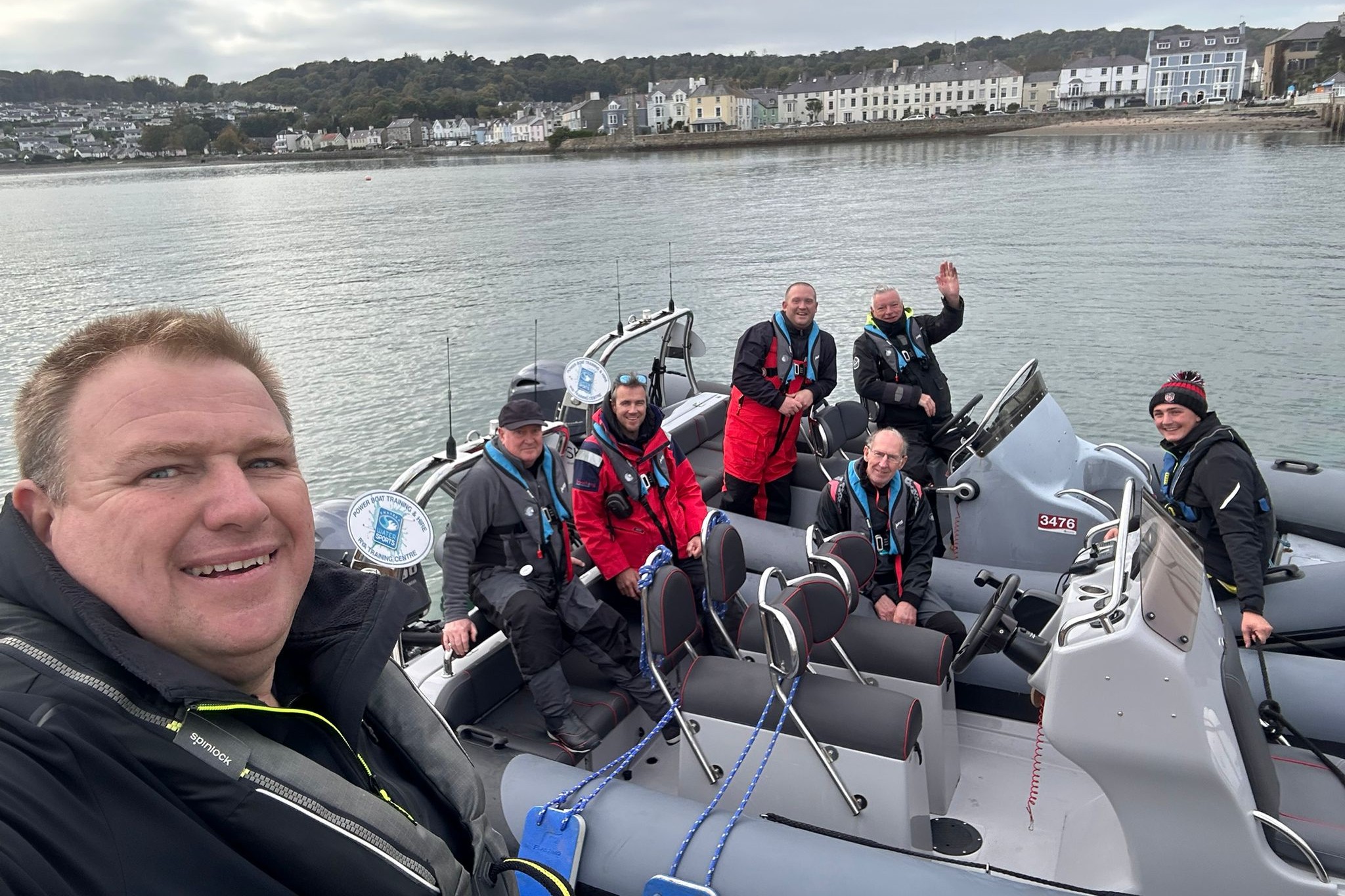 Powerboat trainer taking a selfie with half a dozen course participants behind him waving from moored RIBS next to the dock at the BIG Weekend. 