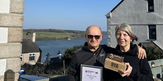Moley and Mandy Morsley with their Welsh Sailing Impact Award on a sunny day in Port Dinorwic with houses and the sea in the background.
