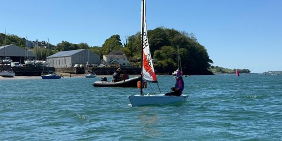 Young sailor on the sea in the sunshine for a Dragon Series event at Port Dinorwic SC in Wales with coach boat nearby, blue waters and sky and beautiful shoreline in the background.