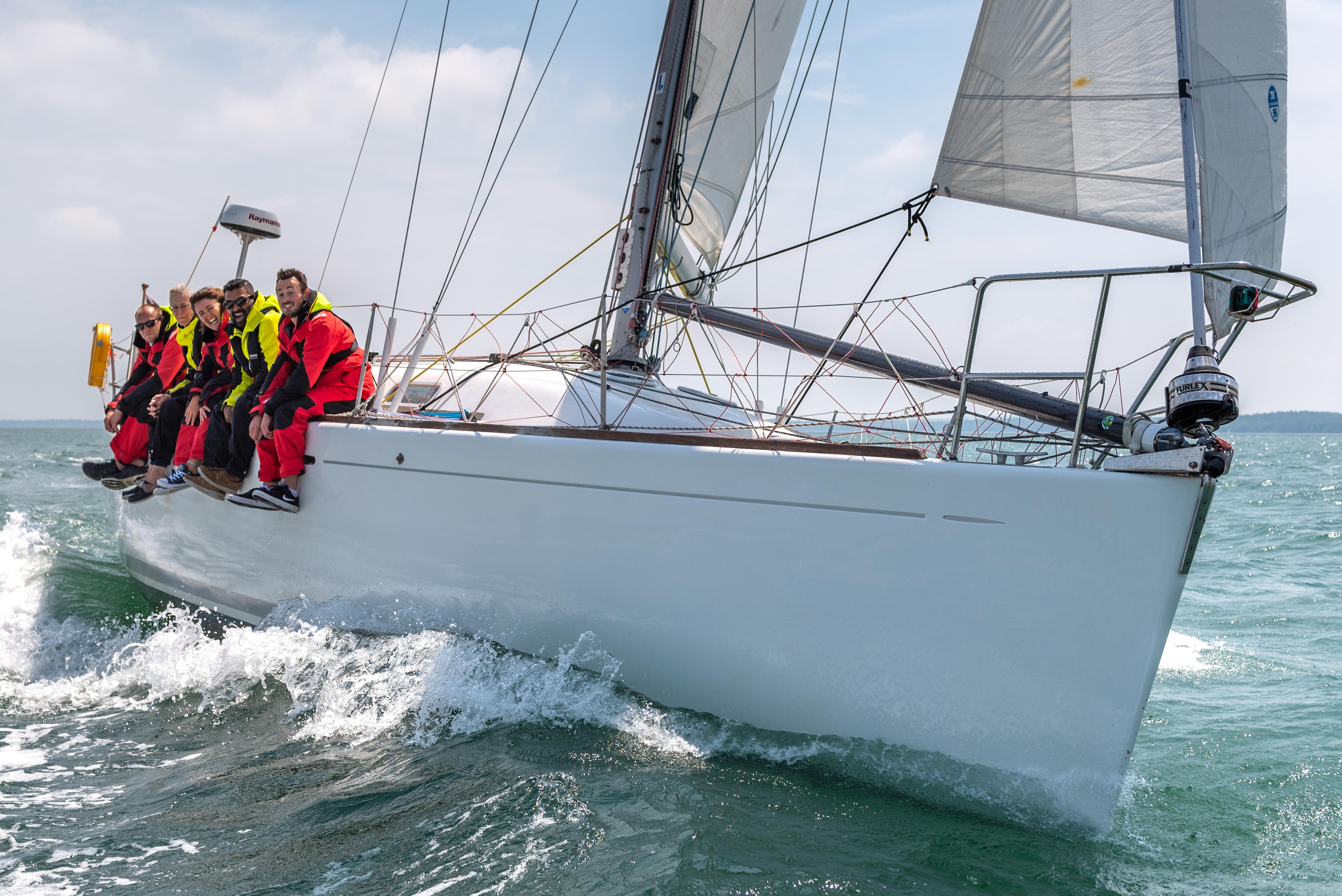 numerous people sat over the side of a sailing yacht whilst sailing on the ocean