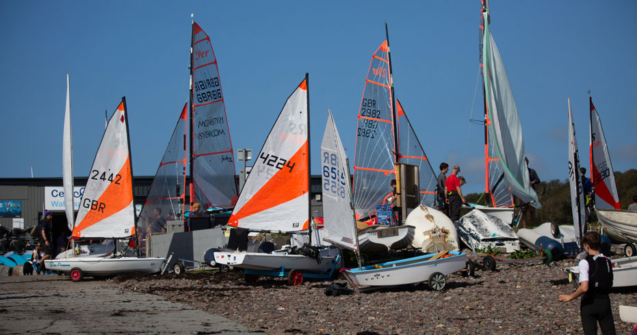 Long shot of orange sailboats and windsurfers on the shore
