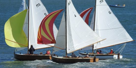 Three dayboats with colourful spinnakers on a sunny day competing in the Menai Strait Regattas in North Wales.