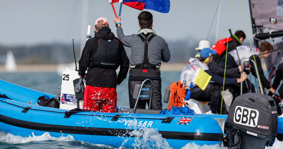 A image with two men on a boat with one being a umpire holding a red flag
