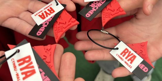 Hands of young sailors holding up the new Welsh Sail / Hwyl Cymru Awards keychain.
